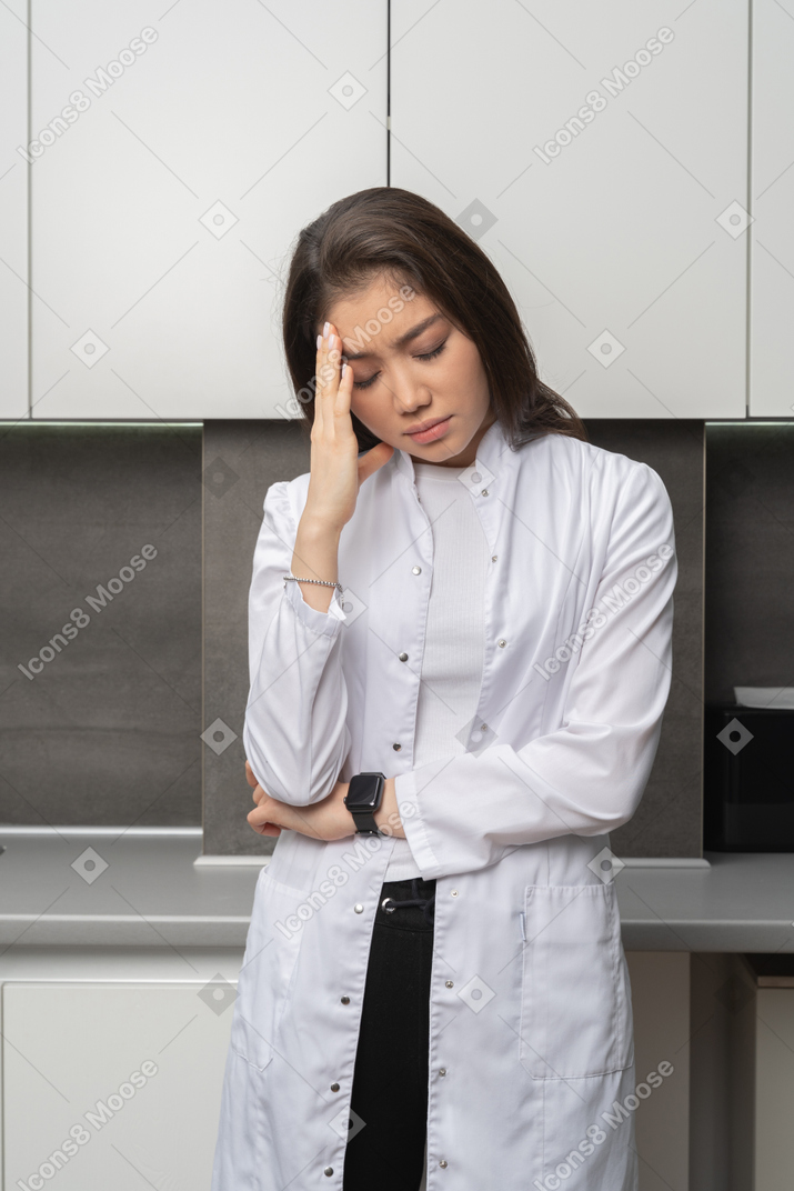 Front view of tired female doctor looking down and touching forehead