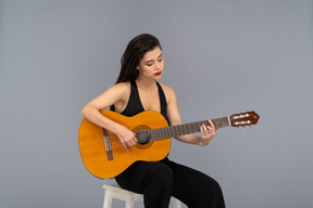 Front view of a sitting young lady in black suit playing guitar