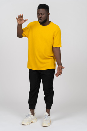 Vue de face d'un jeune homme à la peau foncée en t-shirt jaune montrant la taille de quelque chose