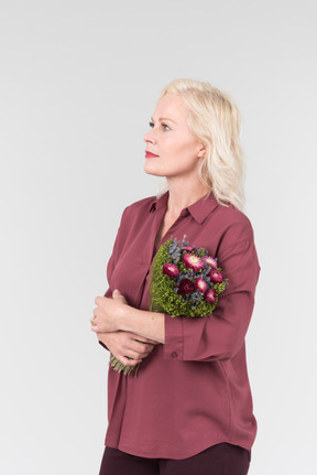 A nice-looking middle-aged blonde woman in a burgundy shirt and with a simple bouquet of flowers in her hands