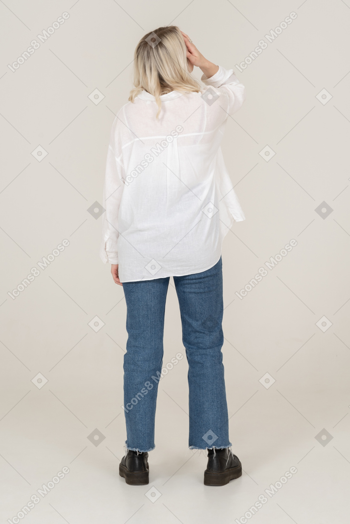 Back view of a blonde female in casual clothes standing still and hiding face