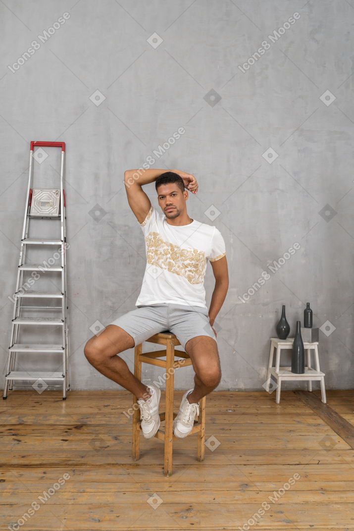 Young man sitting on chair with one arm raised overhead