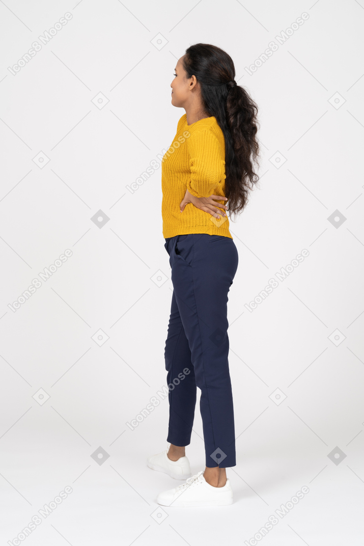 Vista laterale di una ragazza in abiti casual in posa con le mani sui fianchi