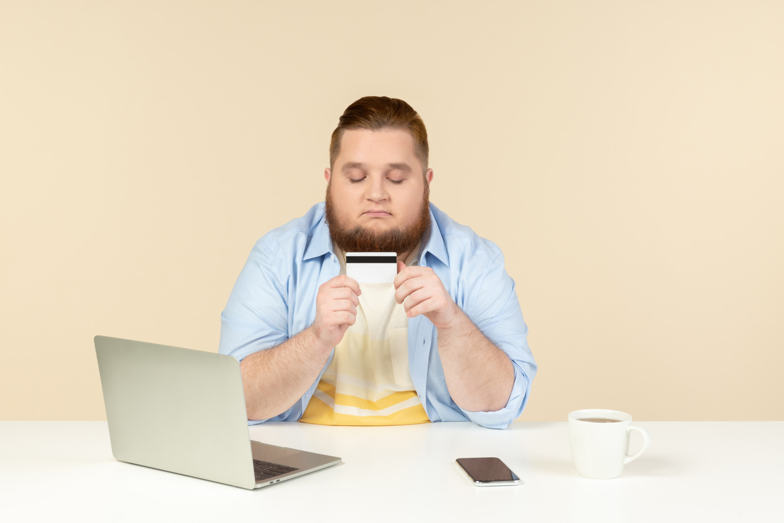 Young overweight man sitting at the table and looking at bank card