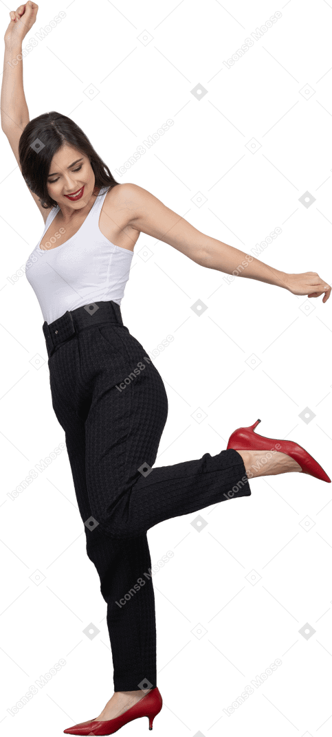 Vista lateral de una mujer joven feliz en ropa de oficina bailando y levantando la mano