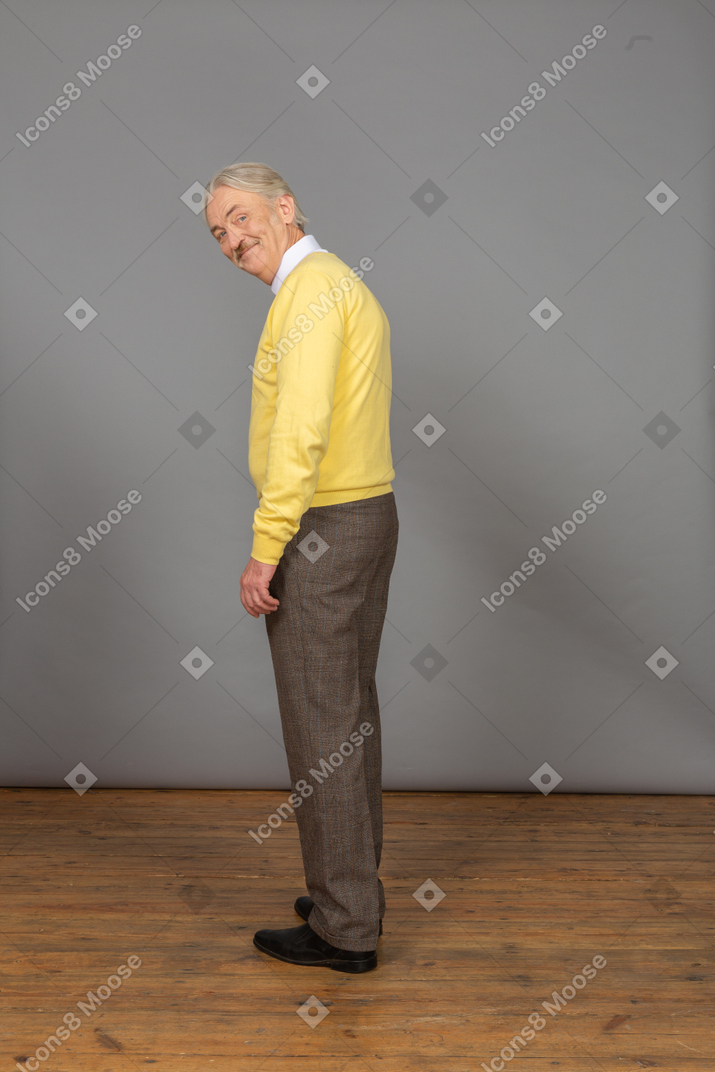 노란색 스웨터를 입고 카메라를 보면서 웃고있는 노인의 3/4 후면보기