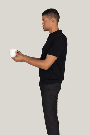 Standing in profile young man in black pants and t-shirt holding cup