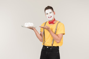 Male clown with cake cream on his face holding a cake