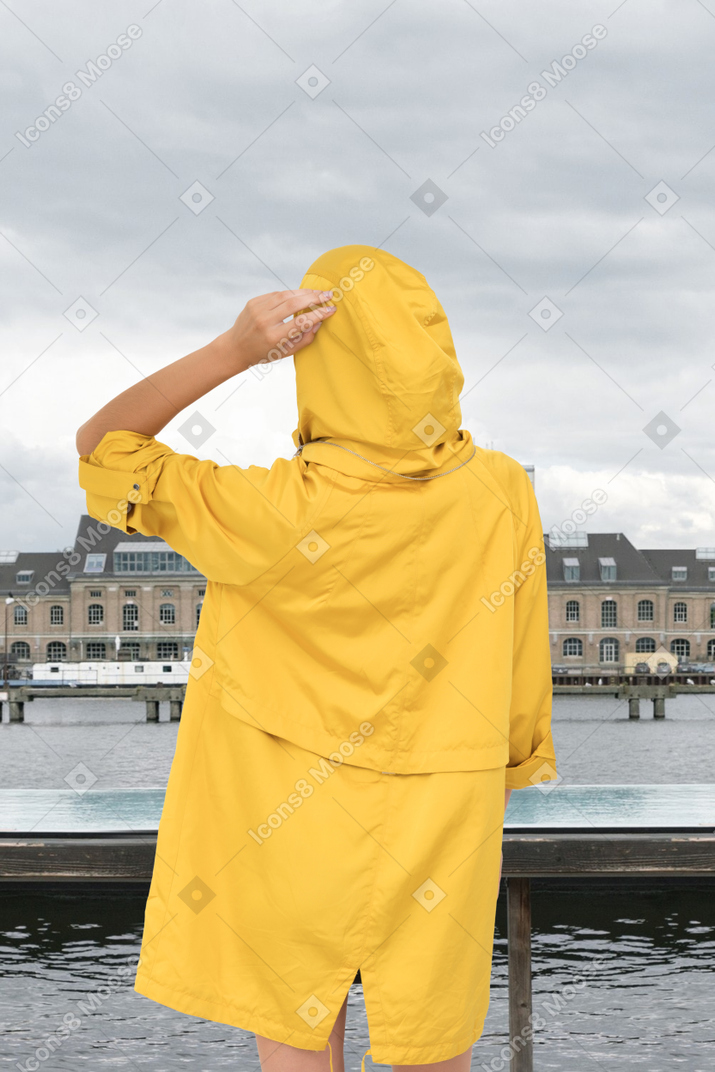 A person in a yellow raincoat looking at a body of water