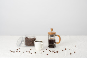 Coffee in french press, large cup of coffee, jar with coffee beans and scattered coffee beans