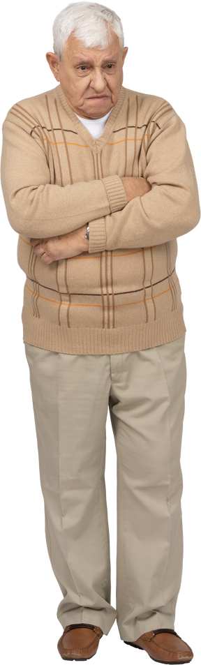 Vista frontal de un anciano gruñón con ropa informal de pie con los brazos cruzados