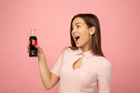 Amused girl  holding a bottle glass and pointing at something