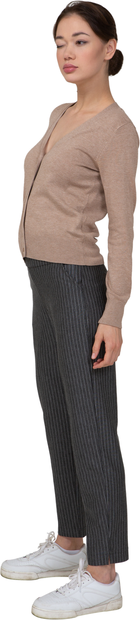 Vista di tre quarti di una giovane donna ammiccante in pullover e pantaloni che mette la mano sul fianco