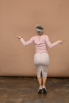 カジュアルな服装でジャンプして腕を広げている女性の背面図