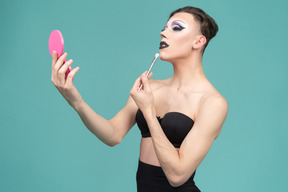 Drag queen aplicando maquiagem enquanto se olha no espelho