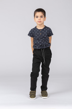 Vista frontal de um menino em roupas casuais em pé com as mãos atrás