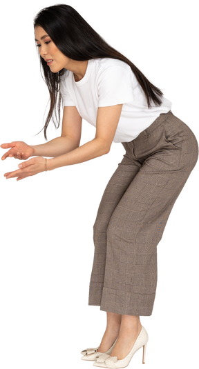 Vista di tre quarti di una giovane donna interrogativa in calzoni e maglietta che alza le mani e si china