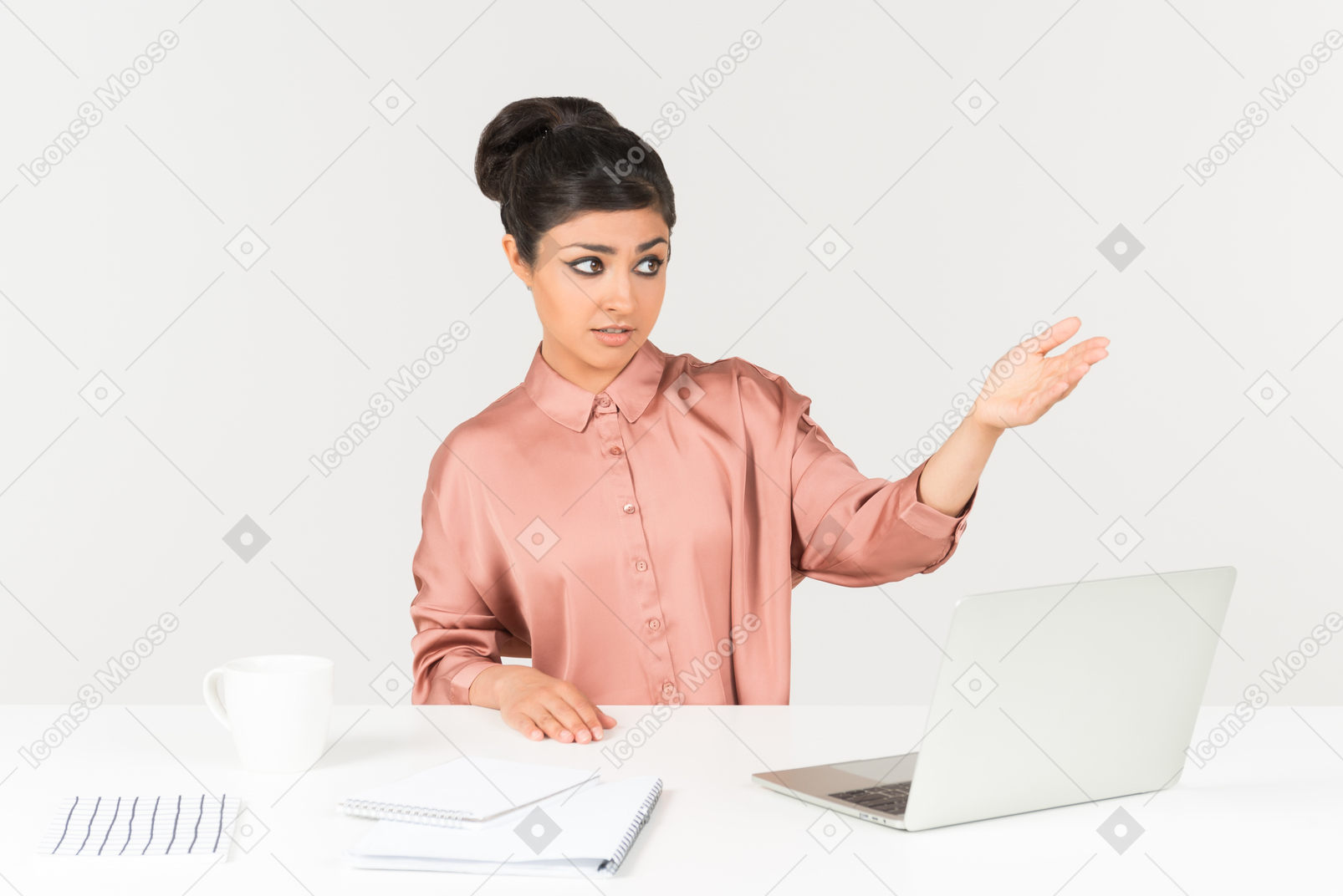 Young indian office worker sitting at the office desk and pointing forward