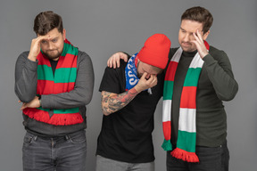 Front view of three sad male football fans touching head