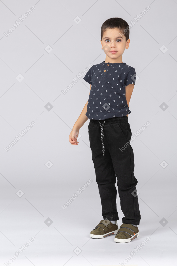 Front view of a cute boy posing with hand behind back and looking at camera