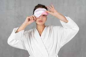 Woman in bathrobe with sleep mask covering one eye