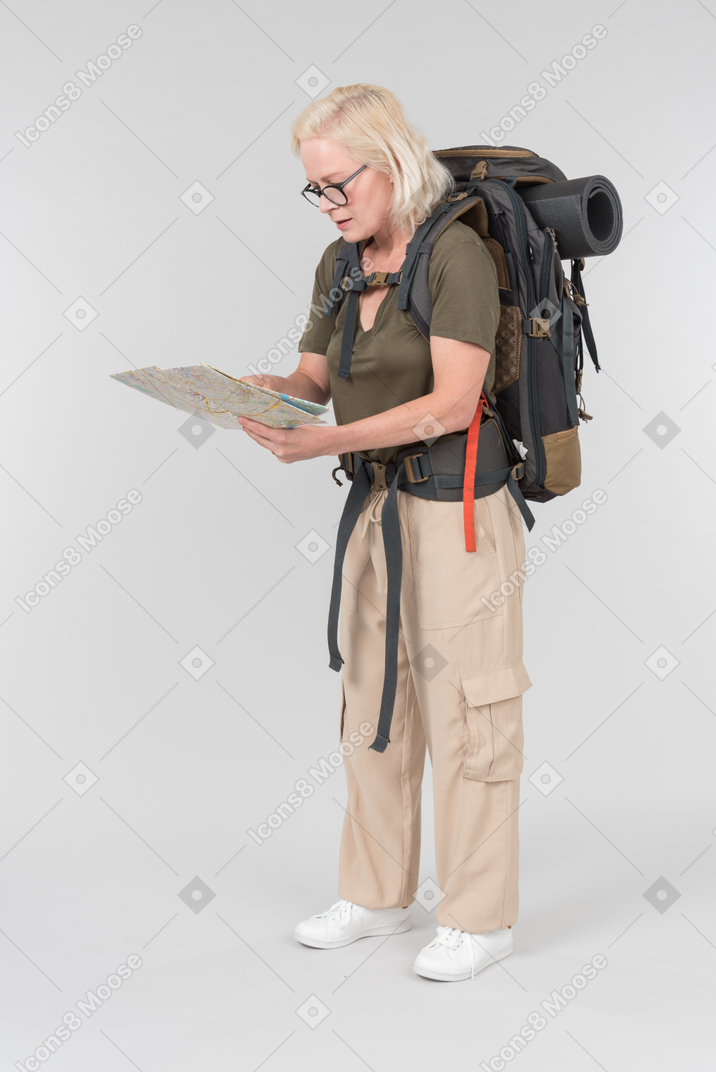 Mature female tourist carrying backpack and looking carefully on map she's holding