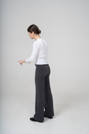 Vue latérale d'une jeune femme en pantalon noir et chemisier blanc pointant du doigt