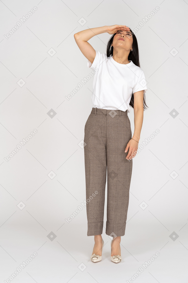 Front view of a young lady in breeches and t-shirt raising hear hand while looking up