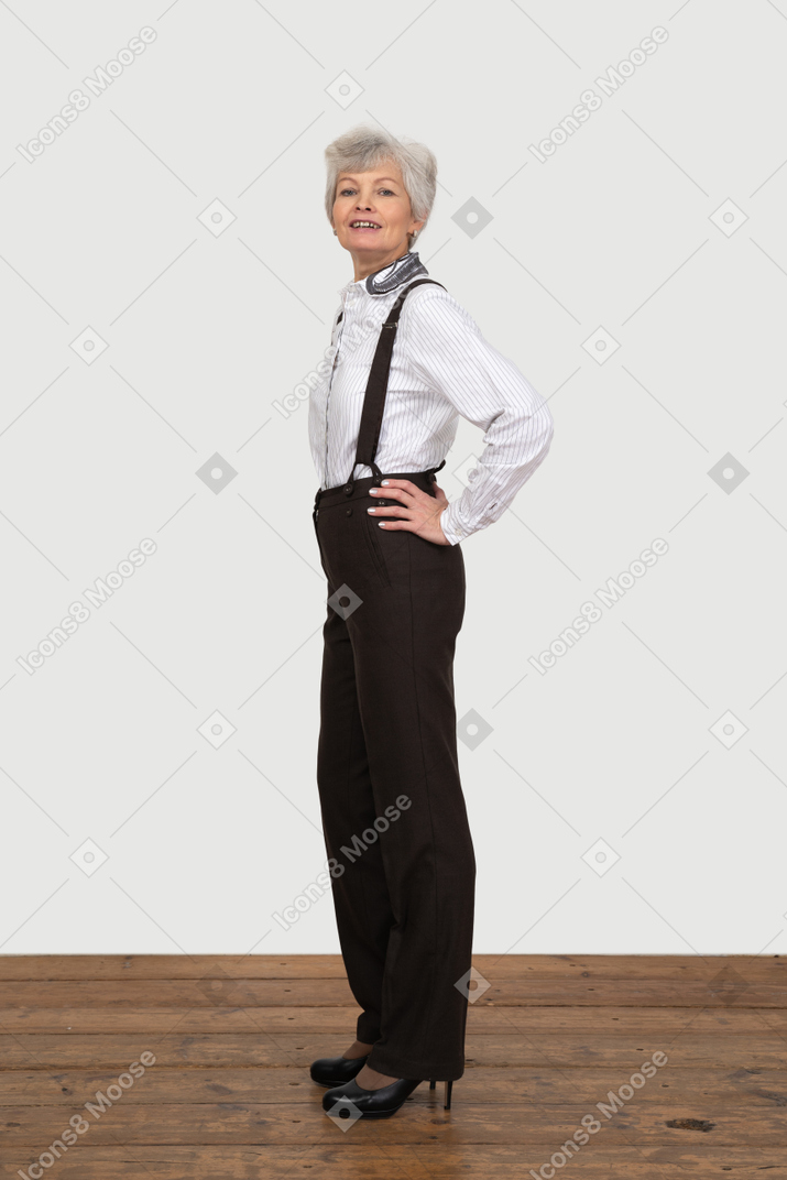 Вид сбоку гордой старушки, положившей руки на бедра в офисной одежде