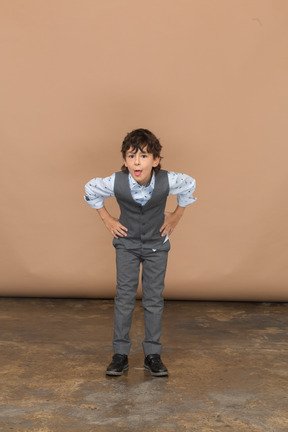 Vista frontale di un ragazzo in giacca e cravatta in piedi con le mani sui fianchi e chinandosi
