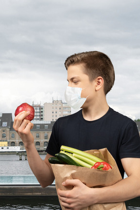 A man holding a bag of vegetables and an apple