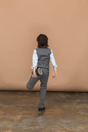 片足で立っているスーツを着た少年の背面図