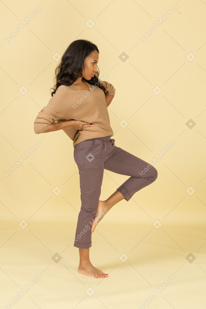 Side view of a dark-skinned young female putting hands on hips while raising leg