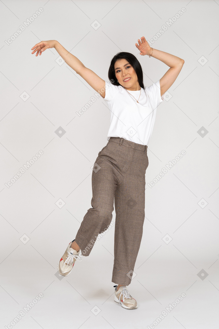 Front view of a dancing young lady in breeches and t-shirt raising hands