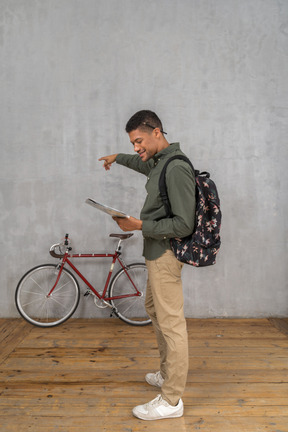 Side view of a man with a backpack looking at a map and pointing aside