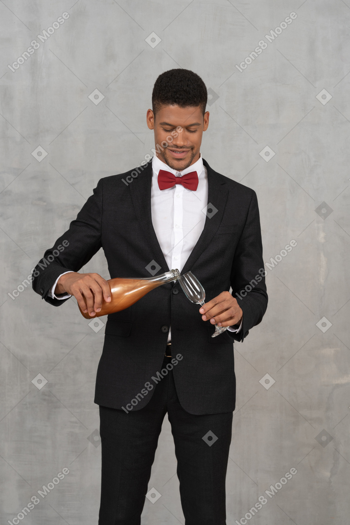 Улыбающийся молодой человек наливает ликер в бокал для флейты