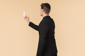 Young man in a black suit and a kippah holding a candle