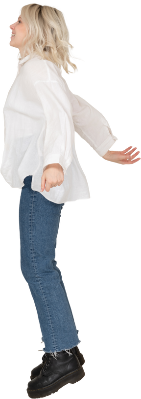 Vista lateral de uma jovem mulher surpresa em roupas casuais pulando e estendendo os braços