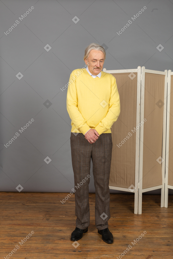 Front view of a confused smiling old man looking down