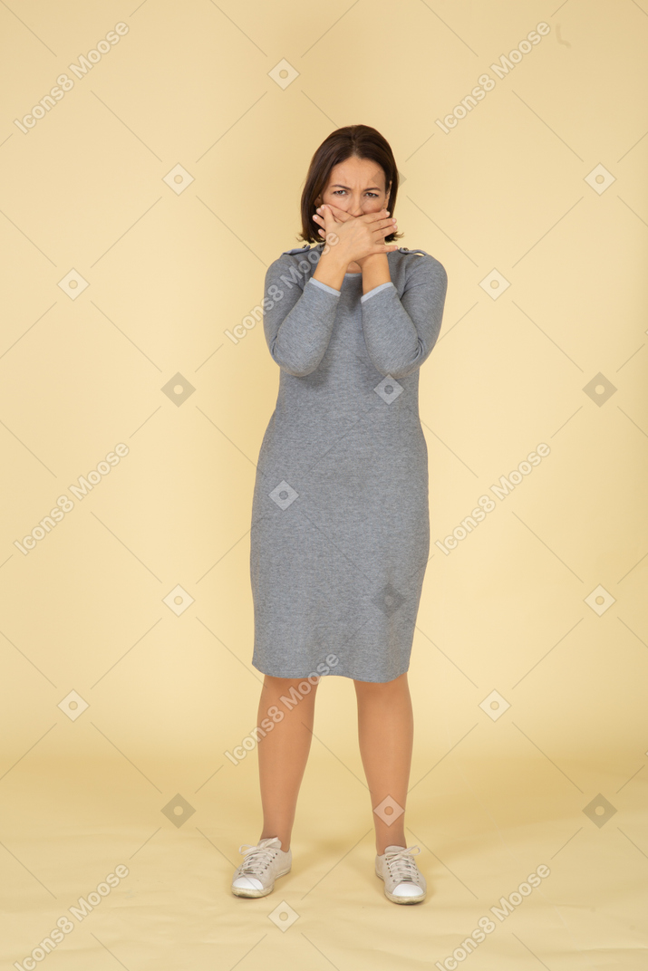 Front view of a woman in grey dress closing mouth with hands