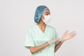 A young woman in a surgical hat and a face mask putting on gloves