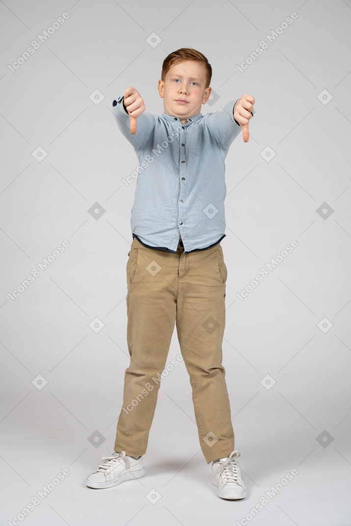 Vista frontal de um menino mostrando os polegares para baixo e olhando para a câmera