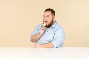 Большой человек сидит за столом и ест мороженое
