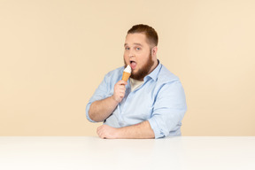 Grande uomo seduto al tavolo e mangiare il gelato