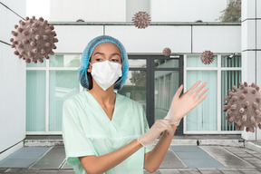 A woman wearing a surgical mask and gloves surrounded by coronavirus molecules