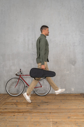 Side view of a man with a ukulele case jumping up