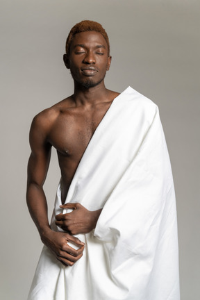 Young black man standing in white sheet and looking at camera