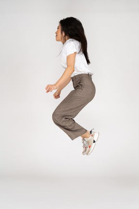 Vista laterale di una giovane donna che salta in calzoni e t-shirt piegare le ginocchia