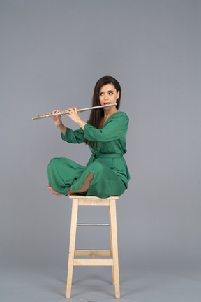 Full-length of a young lady playing the clarinet sitting with her legs crossed on a wooden chair