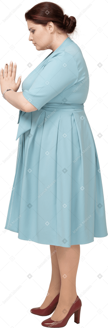Vista lateral de una mujer en vestido azul haciendo gesto de oración